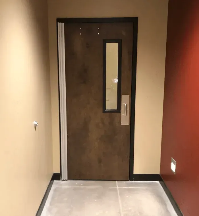 Hallway with a brown door with narrow window, beige walls, and red accent wall.