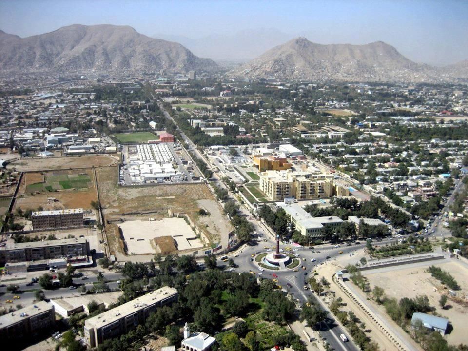 Aerial view of Kabul, Afghanistan, featuring buildings, roads, and mountains in the background under a clear sky.