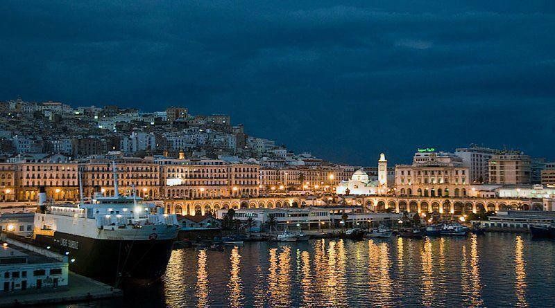 Night view of Algiers, Algeria, with a harbor filled with lights reflecting on the water and city buildings in the background.