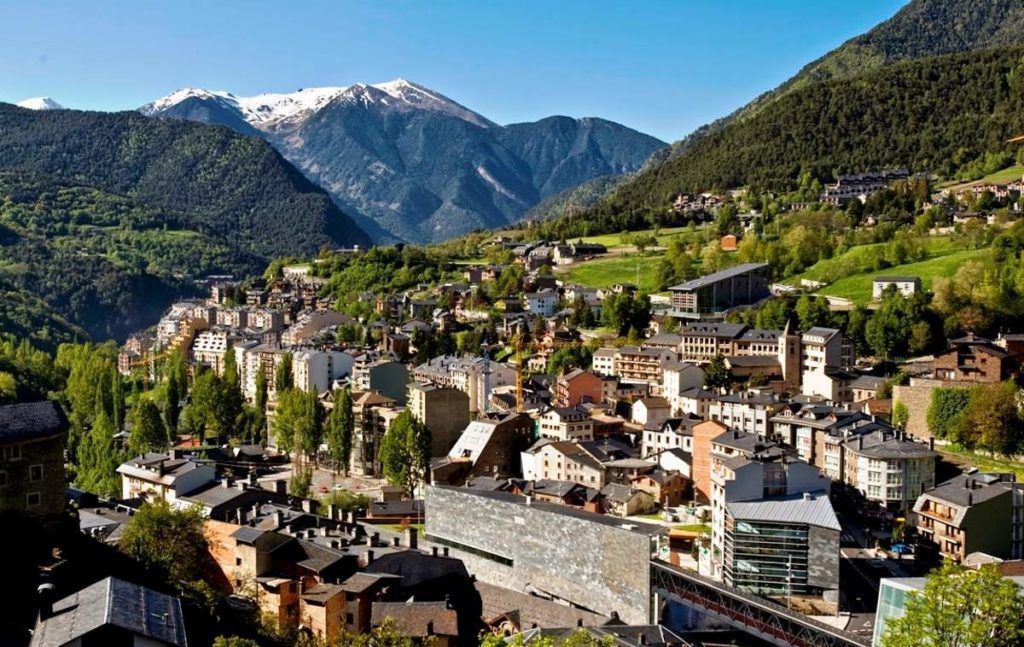 Andorra la Vella cityscape nestled in a valley, with buildings and roads surrounded by mountains and trees.