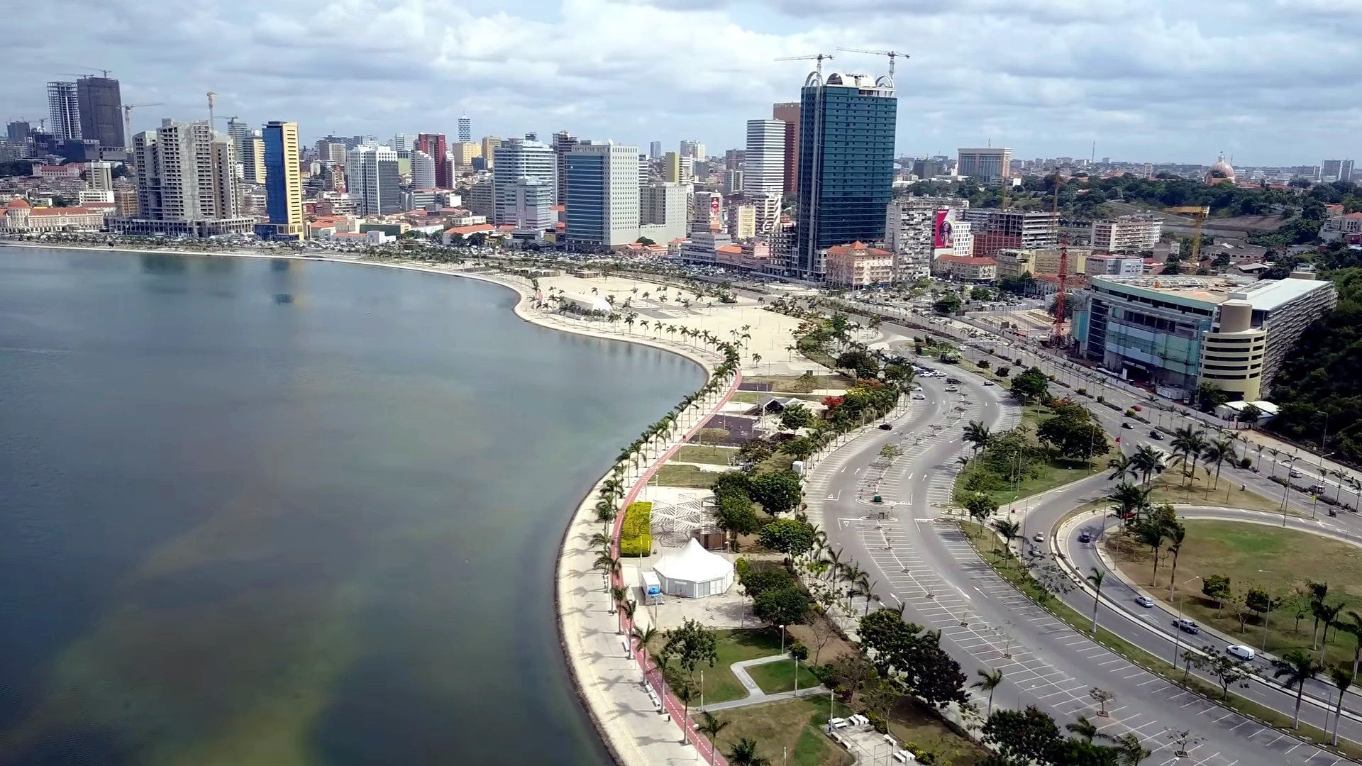 Coastal cityscape of Luanda, Angola. Buildings line the waterfront, a multi-lane highway runs along the shore.