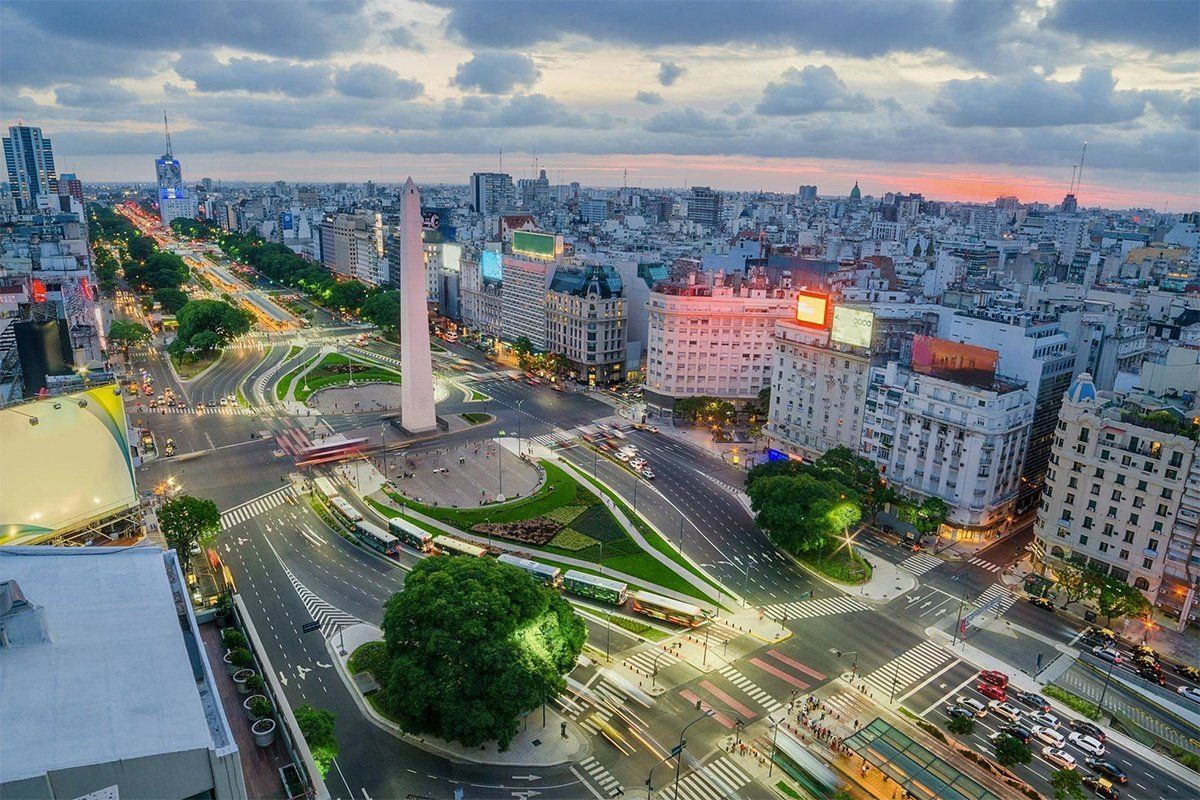Aerial view of Buenos Aires, Argentina at dusk, featuring the Obelisco monument in a wide boulevard with illuminated buildings and city lights.