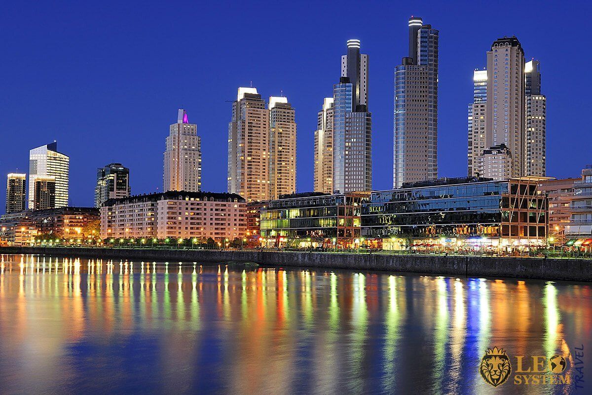 Nighttime cityscape of Puerto Madero, Buenos Aires, Argentina, with illuminated skyscrapers reflected in the water.