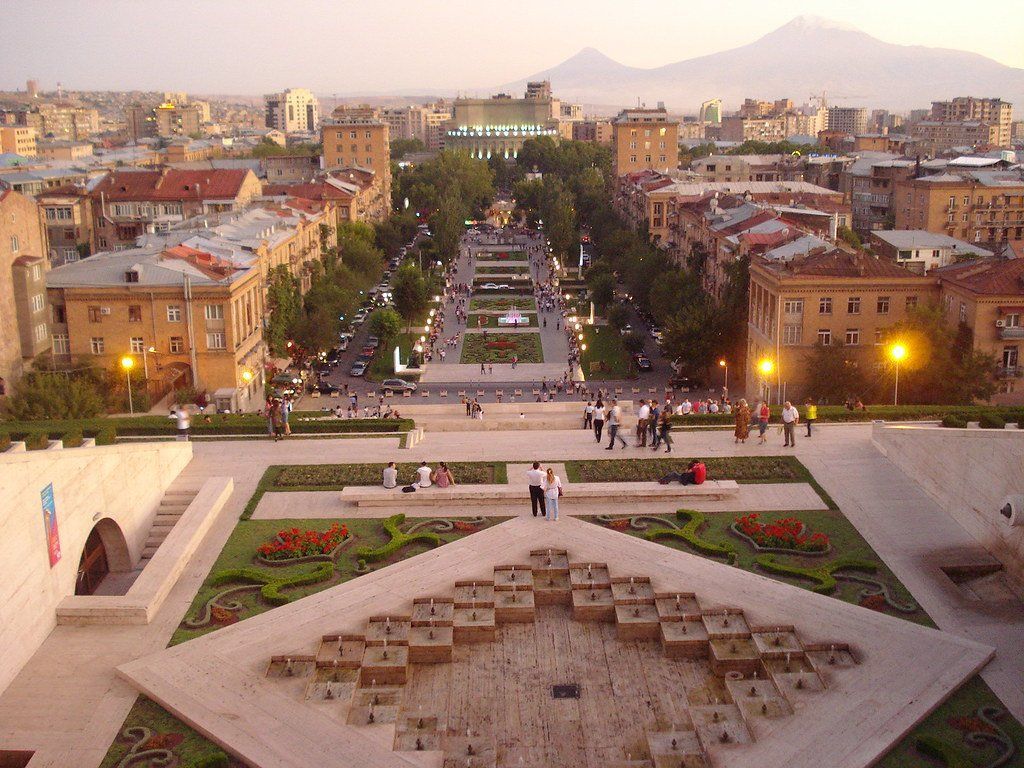 Aerial view of Yerevan, Armenia, with cascading steps, a central parkway, and Mount Ararat in the background at dusk.