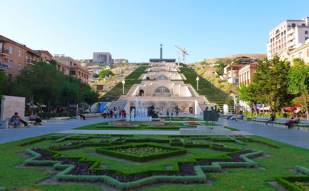 The Cascade complex in Yerevan, Armenia, with terraced steps, fountains, sculptures, and a view of the city. Lush greenery and clear blue sky.