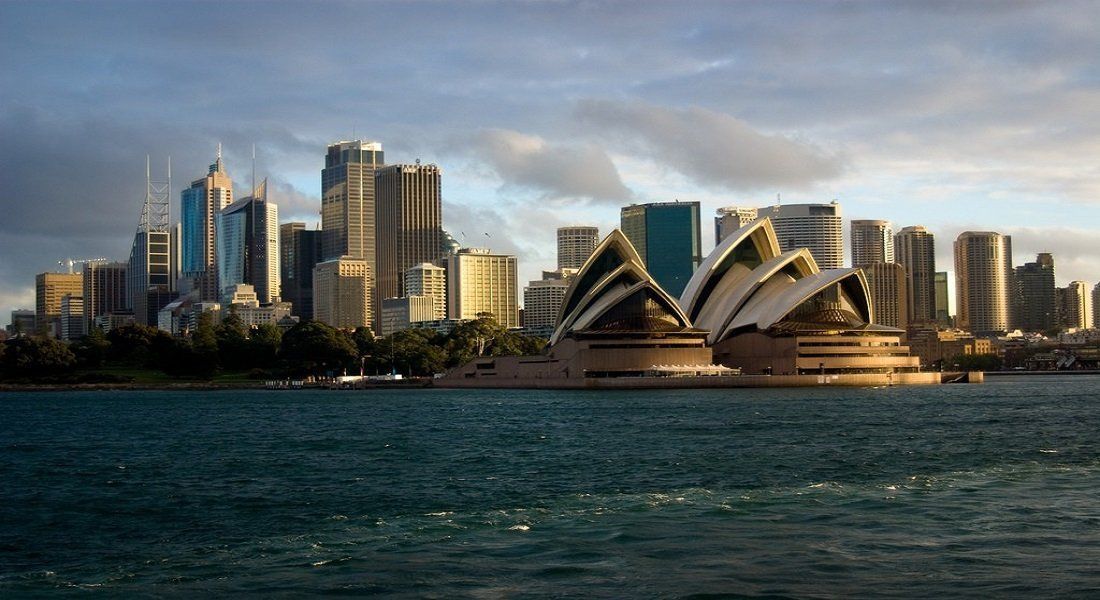 Sydney Opera House and skyline viewed from the water, blue sky, golden light.