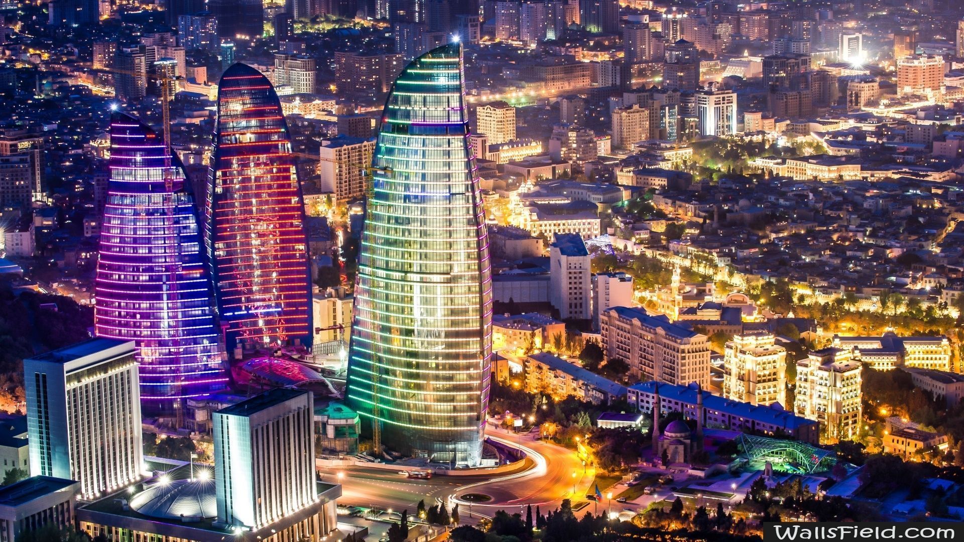 Nighttime view of Baku, Azerbaijan, with the flame-shaped Flame Towers illuminated in purple, red, and green, towering over the city lights.