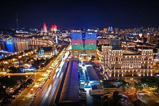 Night view of Baku, Azerbaijan, illuminated with city lights.  The iconic Flame Towers and buildings lit with Azerbaijani flag colors are prominent.