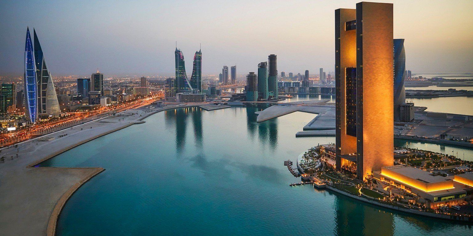 Skyline of Manama, Bahrain, with modern skyscrapers, the Bahrain World Trade Center in the foreground, and a calm blue bay.