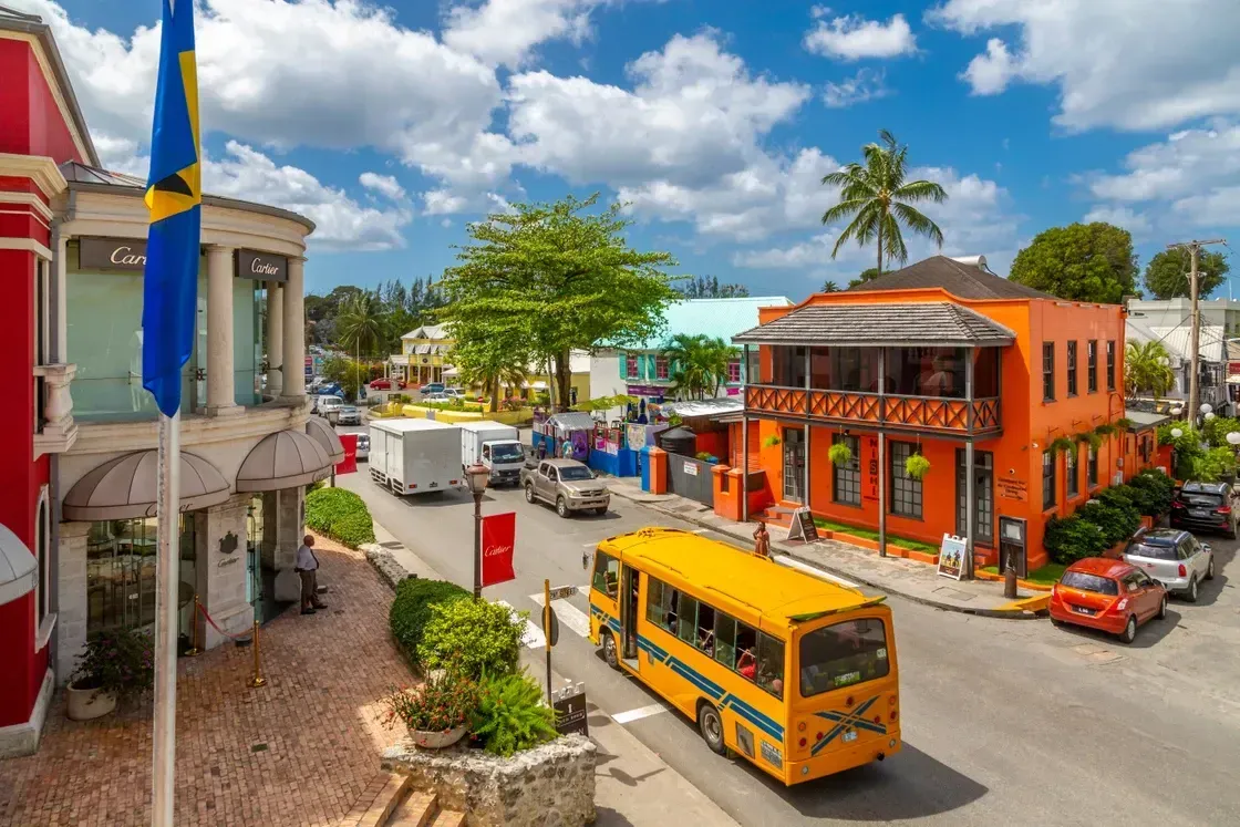 Street scene in Barbados with colorful buildings, a yellow bus, cars, and the Barbados flag.