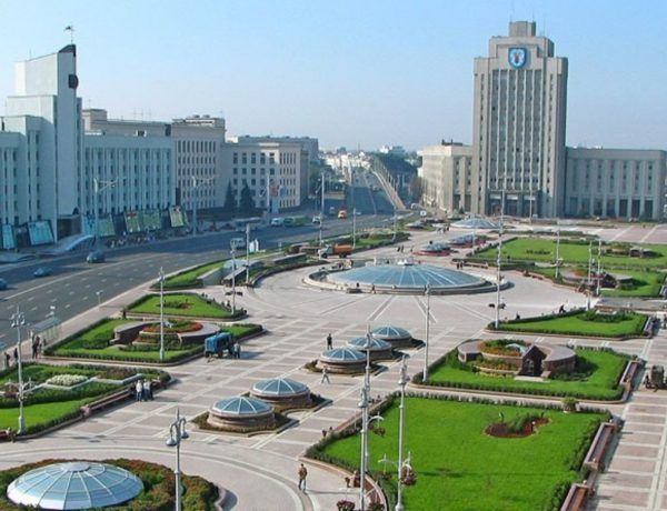 A wide shot of Independence Square in Minsk, Belarus. Buildings and gardens surround a large plaza with glass domes.