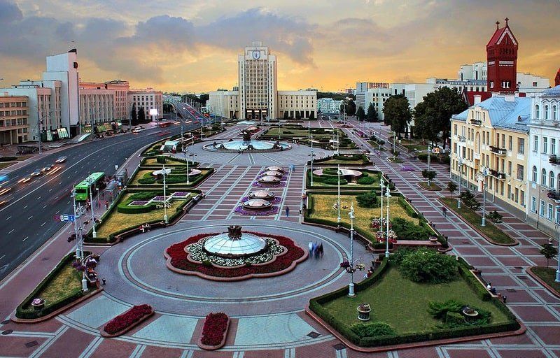 Aerial view of Independence Square in Minsk, Belarus, featuring fountains, gardens, and buildings with traffic along the road.