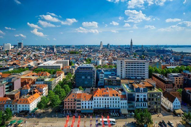 Aerial view of Antwerp, Belgium, showcasing a dense cityscape with buildings of various heights and architectural styles under a blue sky.