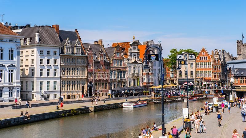 Canal lined with colorful buildings and pedestrians in Ghent, Belgium on a sunny day.