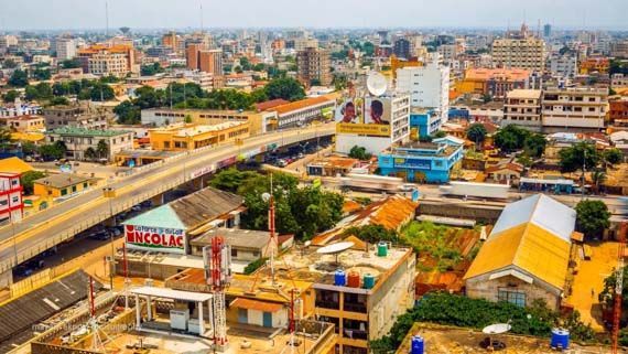 Aerial view of a bustling city, possibly in Africa, with a bridge, colorful buildings, and varying roof heights.