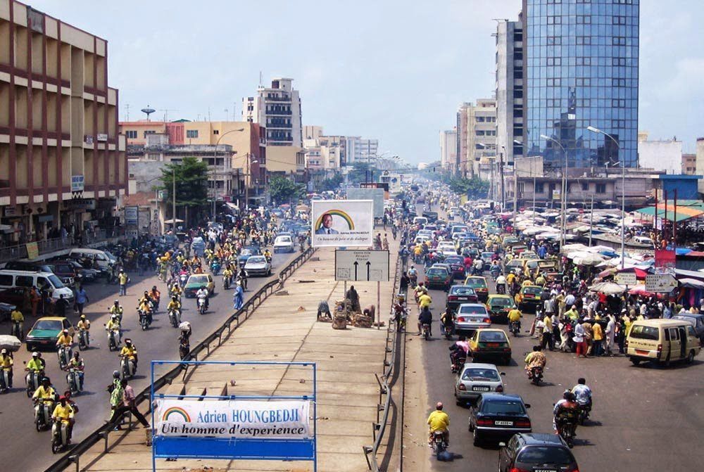 Busy city street in Dakar, Senegal, with heavy traffic including cars and motorcycles. Buildings line the road.