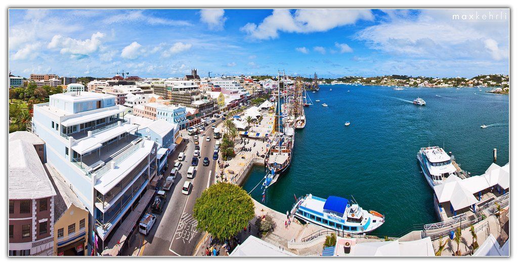 Panoramic view of a waterfront city with boats, buildings, and a blue sky.