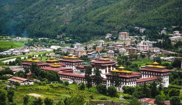 Panoramic view of Punakha Dzong, a fortress-monastery in Bhutan, surrounded by buildings and nestled amidst green mountains.
