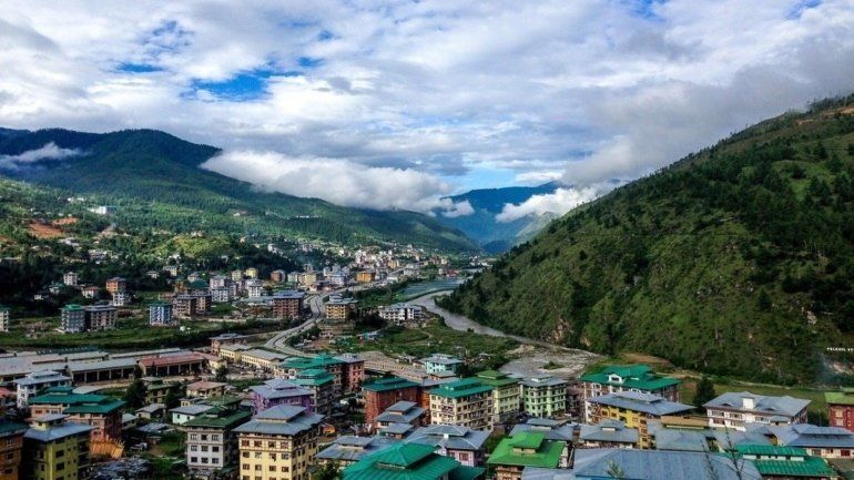 Valley town nestled between green mountains, with buildings and a river under a cloudy sky in Bhutan.