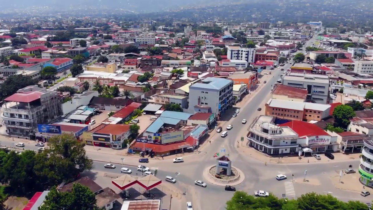 Aerial view of a bustling city with buildings, roads, and a roundabout.  Overcast sky.