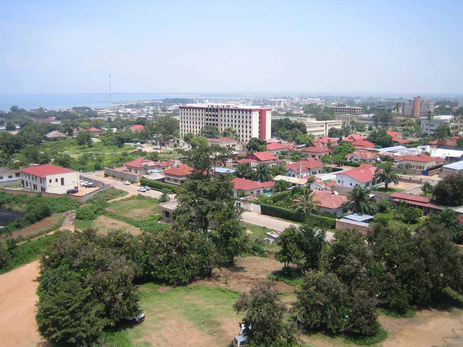 Aerial view of a coastal town with red-roofed houses, a large beige building, and a blue ocean in the distance under a clear sky.