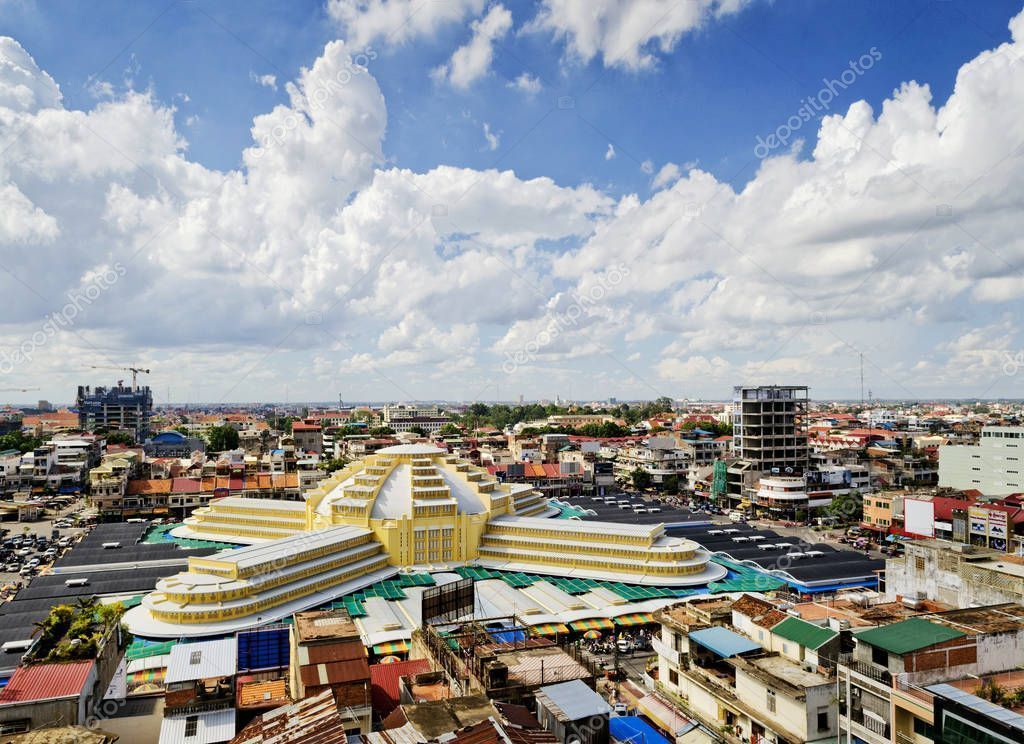 Aerial view of the Central Market in Phnom Penh, Cambodia, a yellow art deco-style building under a partly cloudy blue sky.