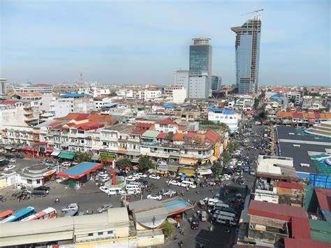 Busy Phnom Penh cityscape with cars and motorcycles on the roads, traditional buildings in the foreground, and two tall modern skyscrapers in the distance.