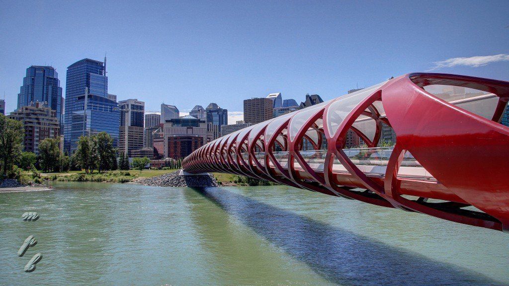 Red Peace Bridge over a river with a city skyline in the background under a blue sky.