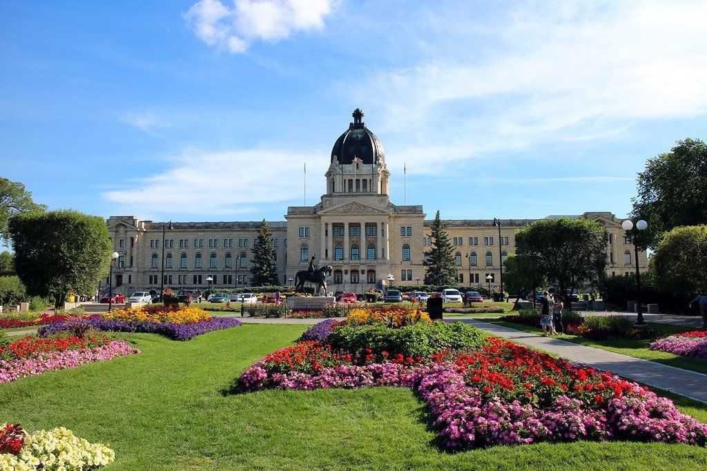 Saskatchewan Legislative Building with colorful flowerbeds in the foreground under a blue sky.