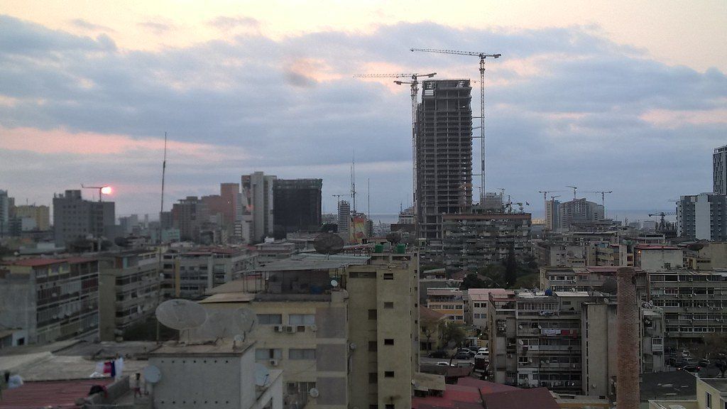 City skyline at dusk, with tall buildings and construction cranes under a cloudy sky.