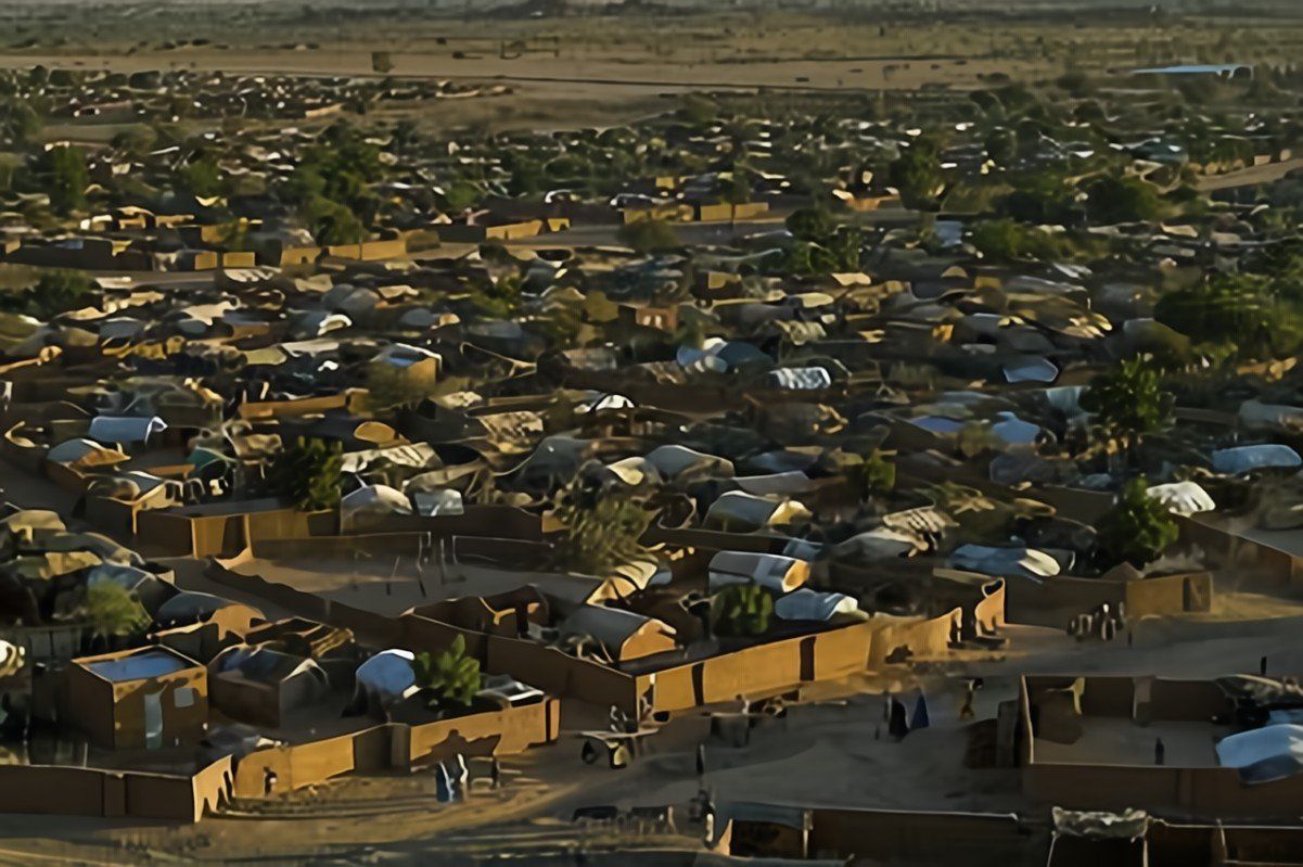 Aerial view of a densely packed village in an arid region, featuring numerous low, mud-brick structures and tents.