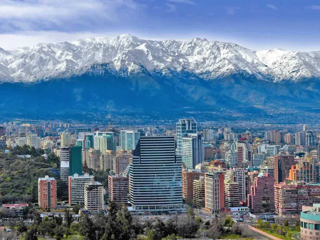 City skyline with modern high-rises against the backdrop of snow-capped mountains and a blue sky.