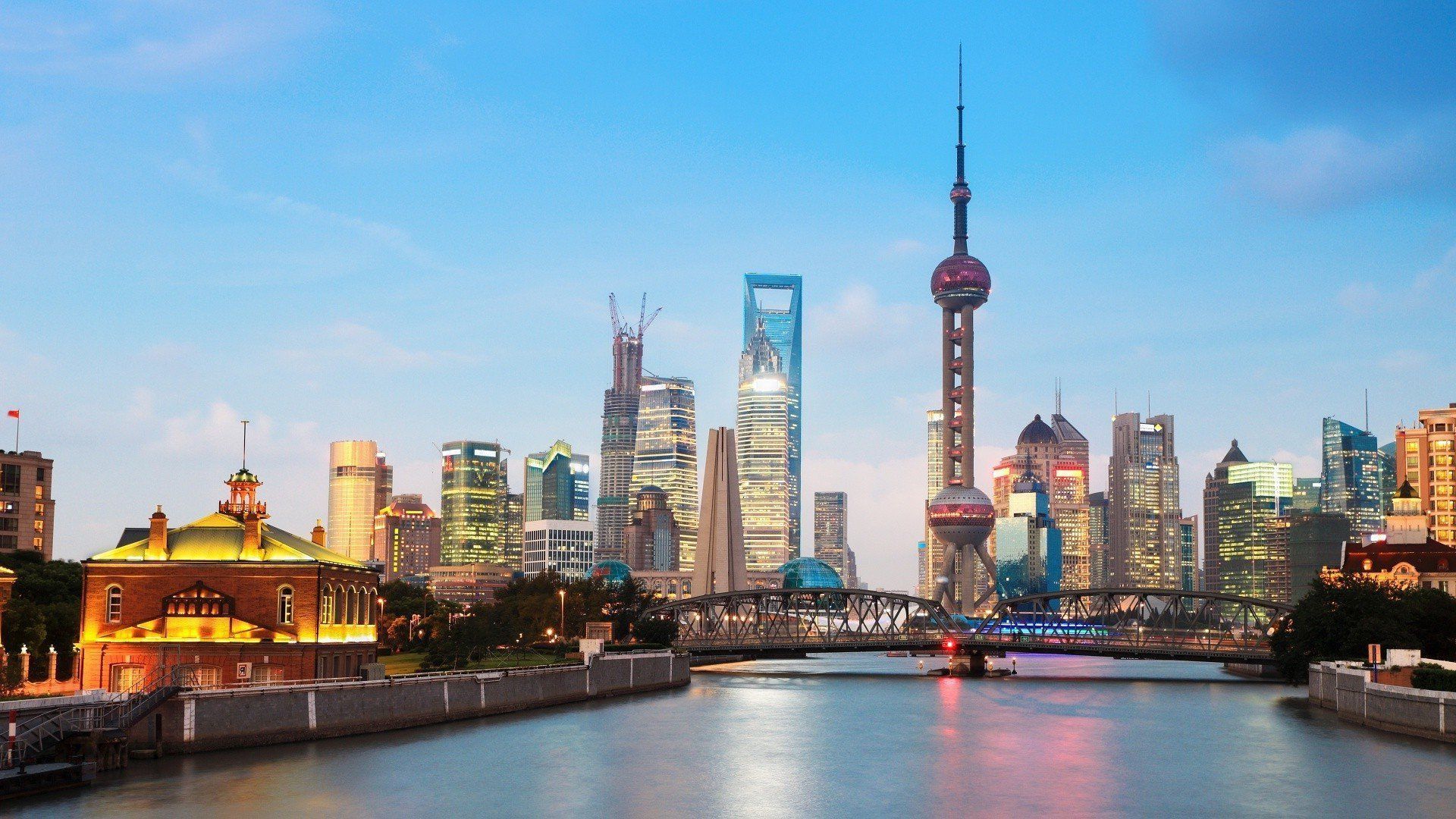 Shanghai skyline at dusk with water in the foreground. Tall buildings and the Oriental Pearl Tower are visible.