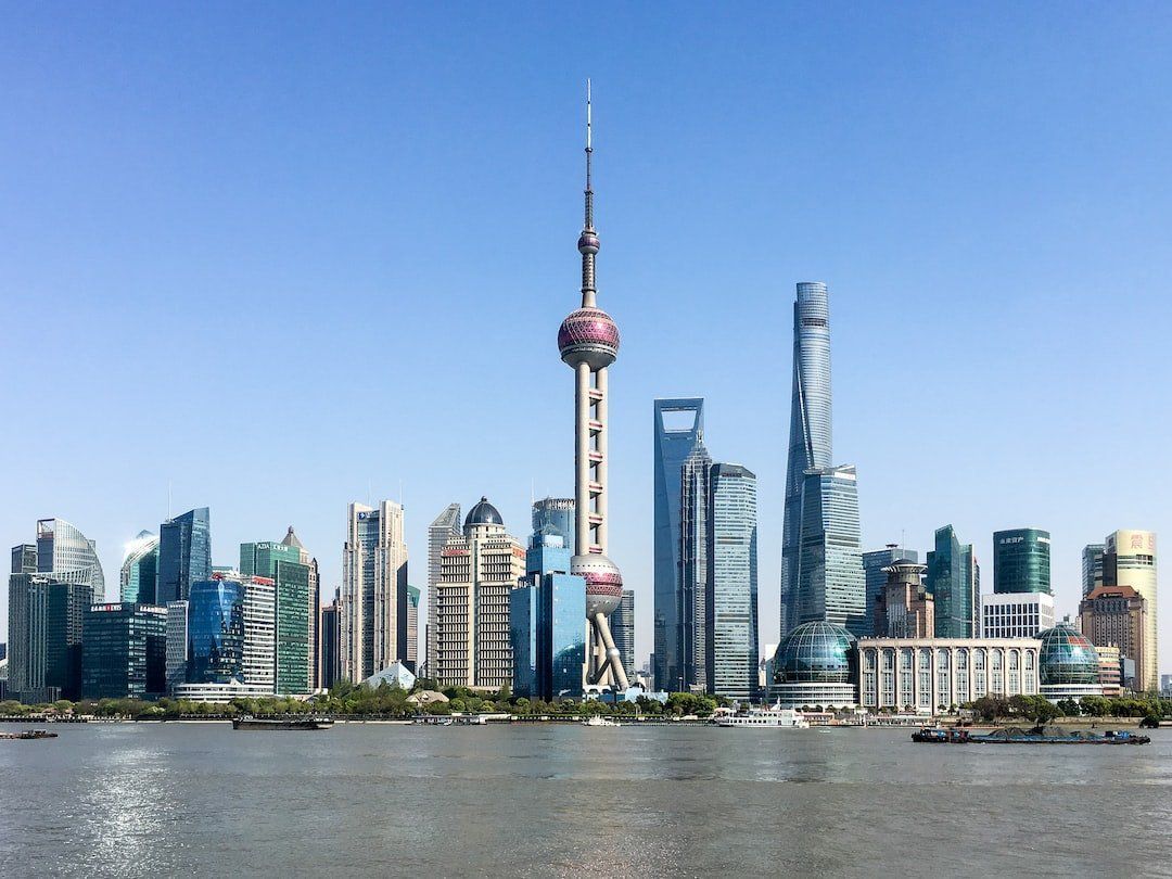 Shanghai skyline with the Oriental Pearl Tower in the center, featuring modern skyscrapers against a blue sky, viewed from across a river.