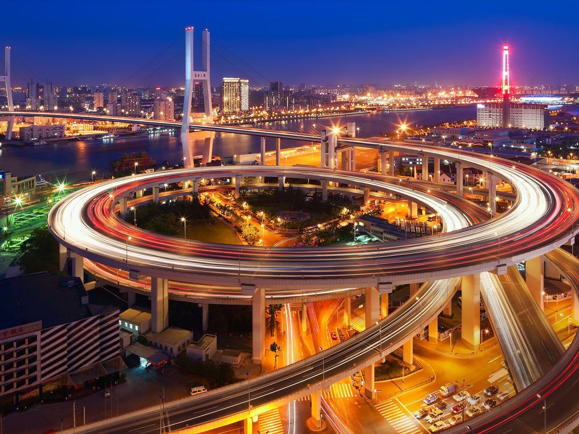 Night view of Shanghai with a spiral highway overpass lit with car lights, and city lights in the background.