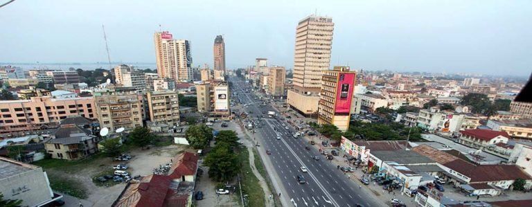Aerial view of a city with a multi-lane highway. Tall buildings and billboards line the road, with a mix of urban and residential structures.