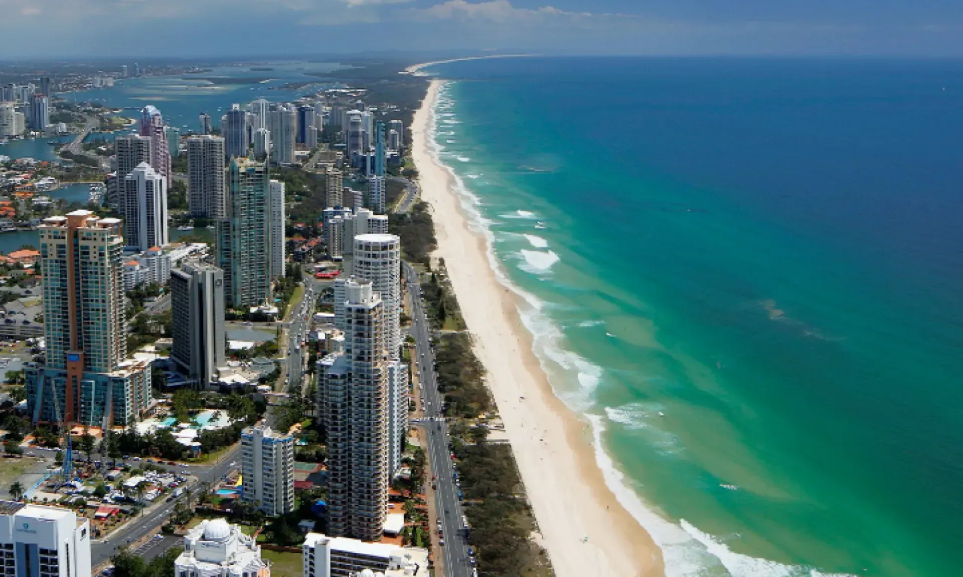 Aerial view of a city with tall buildings next to a long, sandy beach and turquoise ocean.