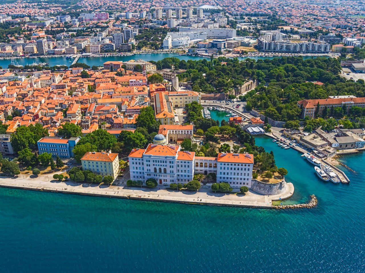 Aerial view of Zadar, Croatia, showcasing the old town with orange rooftops, a waterfront, and turquoise sea.