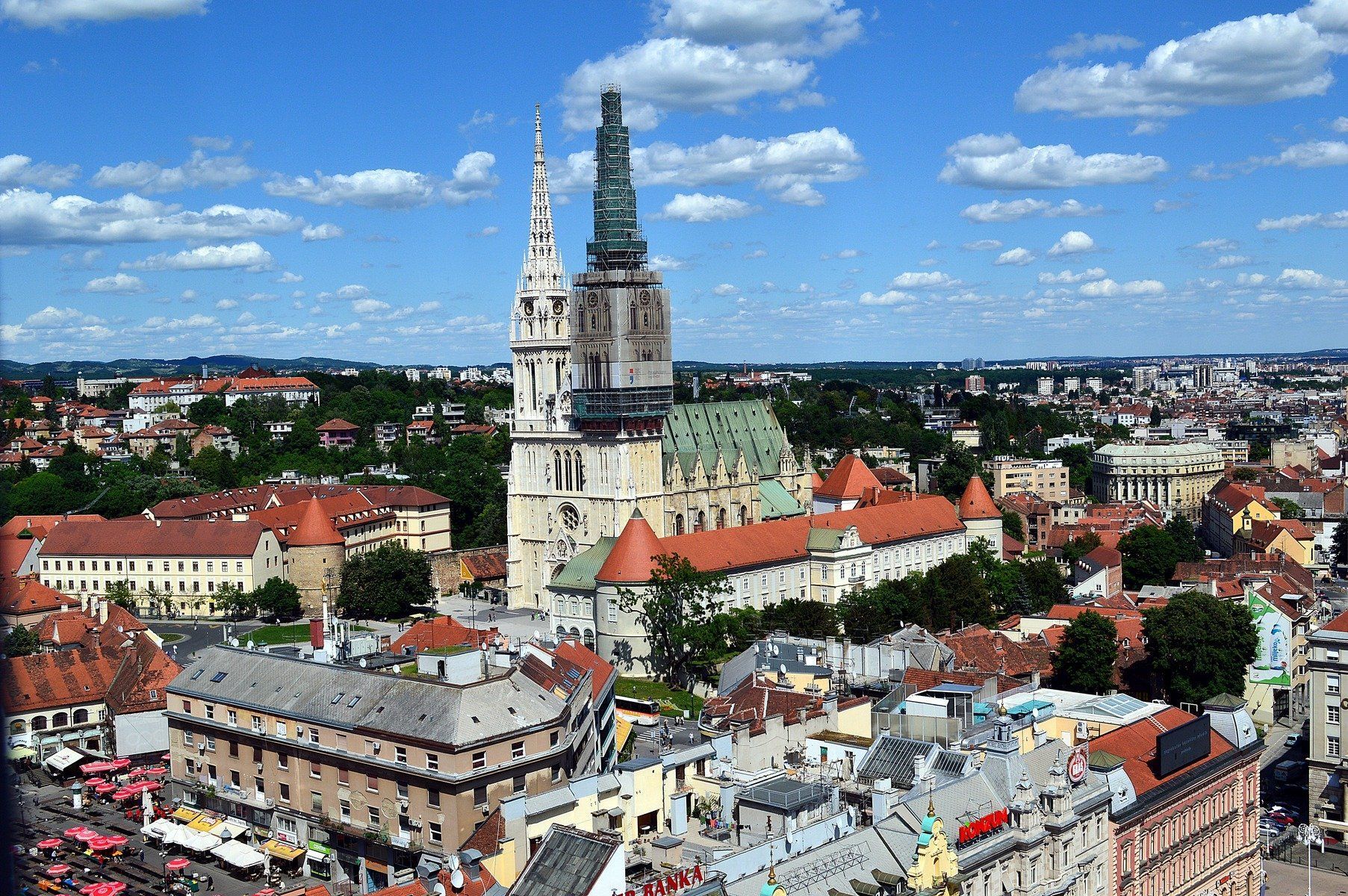 Cityscape of Zagreb, Croatia, dominated by the twin spires of Zagreb Cathedral against a blue sky with puffy white clouds.