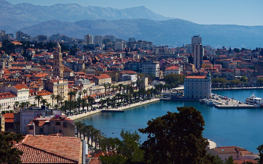 Cityscape of Split, Croatia, with red-tiled roofs, a harbor, and mountains in the background.