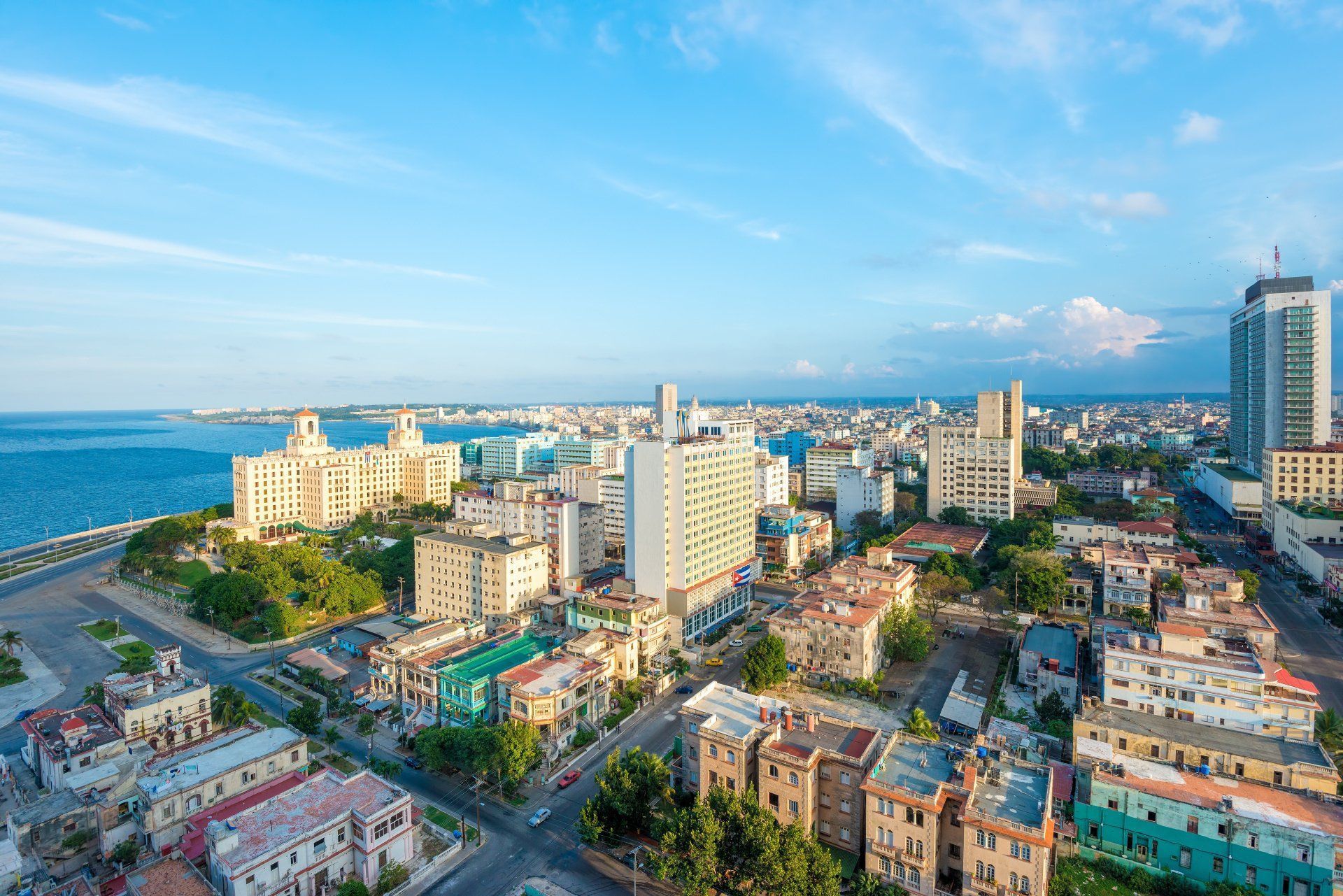 Cityscape of Havana, Cuba, featuring buildings of various heights along a coastline, under a bright blue sky with the ocean in the background.