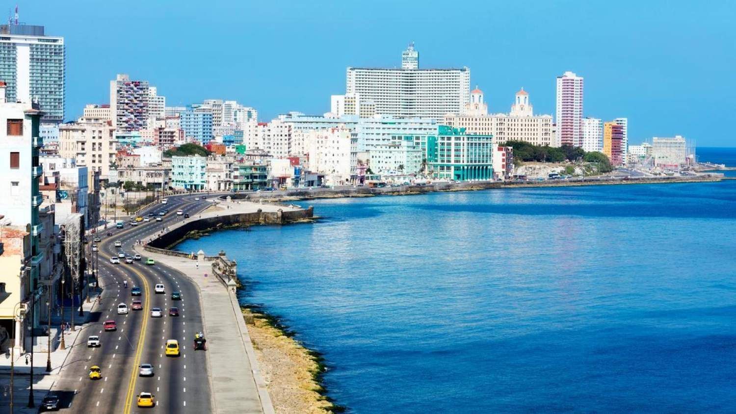 Coastal cityscape of Havana, Cuba, with a wide road along the sea, colorful buildings, and blue water under a clear sky.
