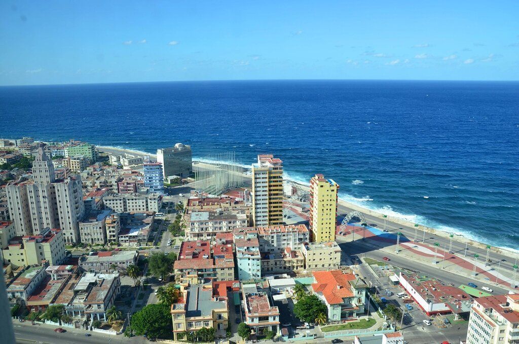 Aerial view of Havana, Cuba, with buildings of various colors along the coast under a bright blue sky and the ocean.