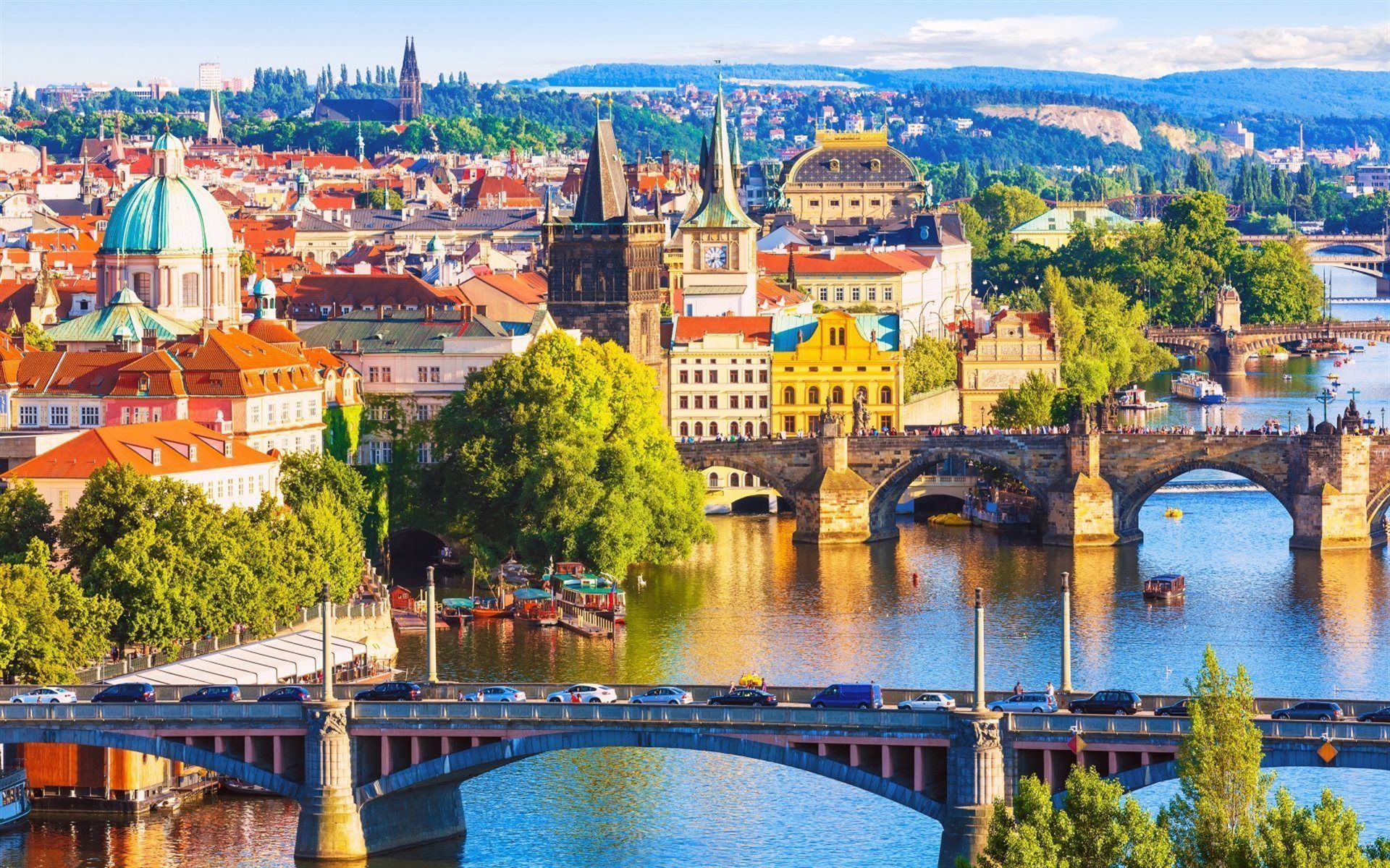 Prague cityscape with colorful buildings along a river, multiple bridges spanning the water, and a blue sky.