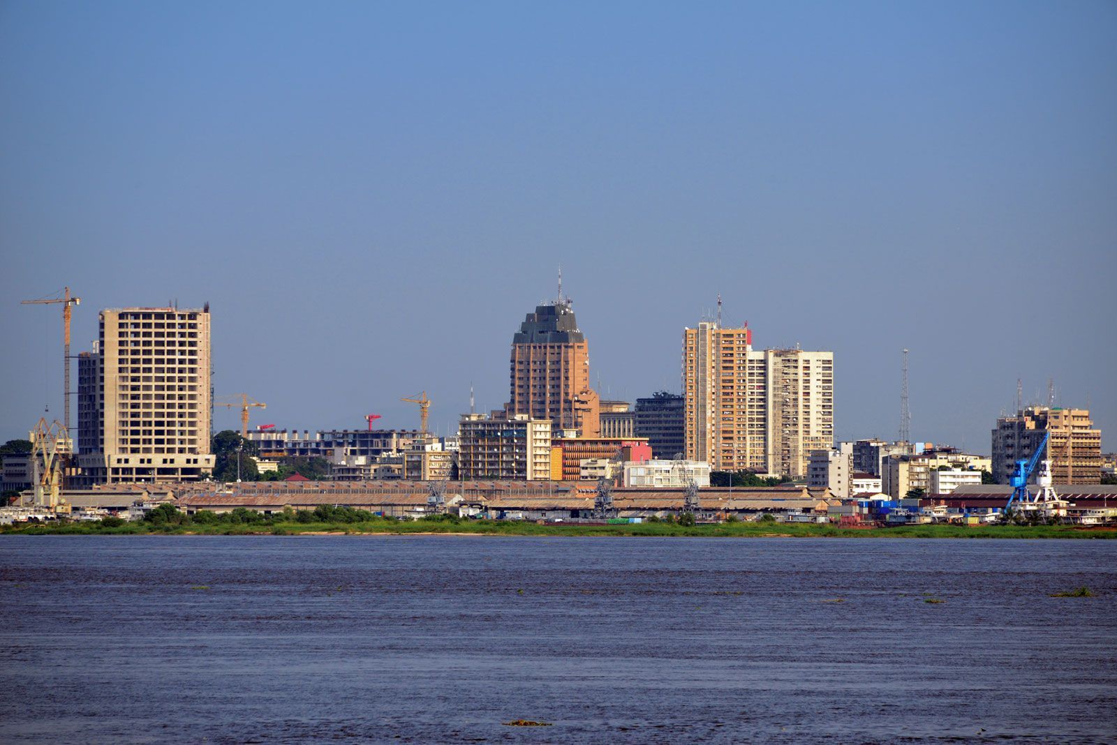 Skyline of Brazzaville, Congo, with buildings of varying heights along a river, under a clear blue sky.