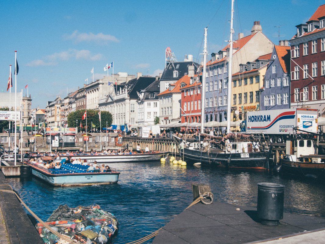Colorful buildings line a canal in Copenhagen, with boats and a bright blue sky.