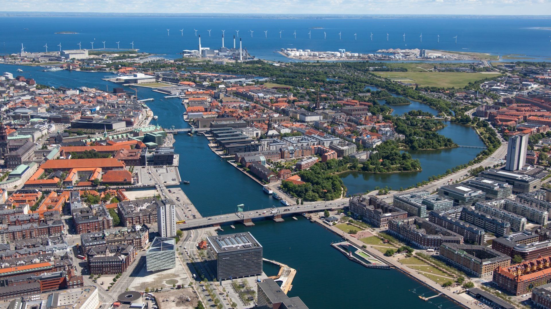 Aerial view of Copenhagen, Denmark, showing canals, buildings, and a distant coastline with wind turbines.