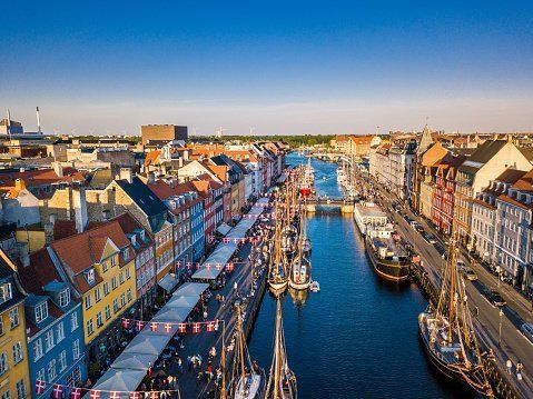 Aerial view of Nyhavn harbor in Copenhagen, Denmark. Colorful buildings line the canal, with boats and crowds visible.