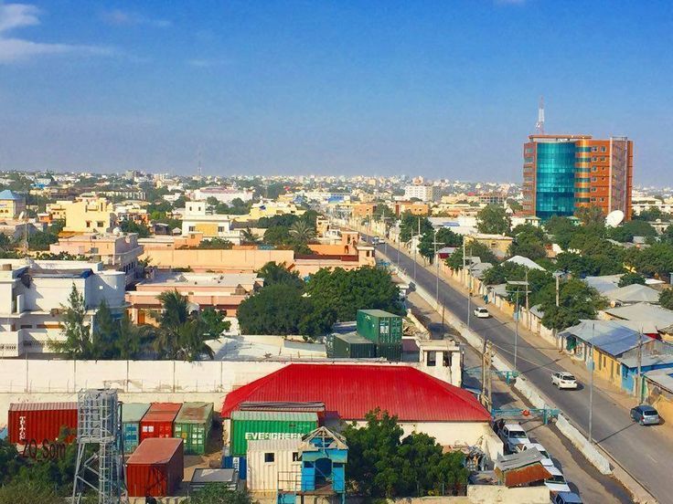 Overhead view of Mogadishu, Somalia, with a mix of low buildings and a modern skyscraper. Bright blue sky.