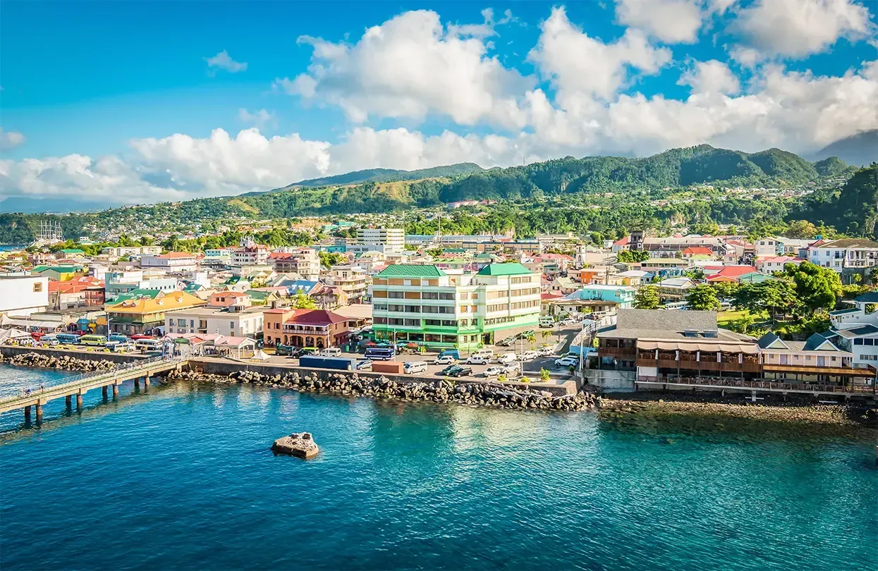 A vibrant coastal town with colorful buildings sits next to a blue ocean, under a blue sky and green mountains.